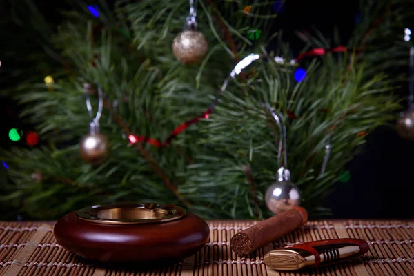 Noel ağacının arka planında, üzerinde puro ve çakmak olan bir kül tablası..