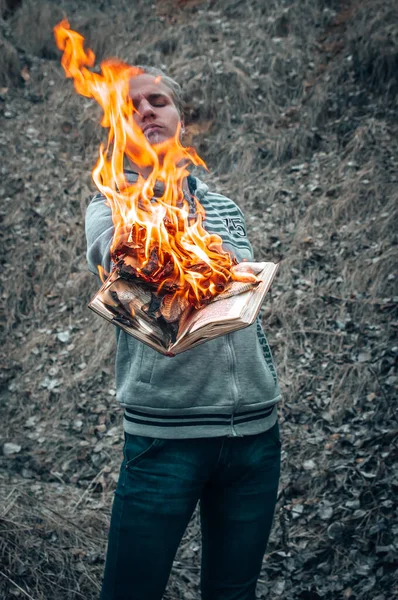 Um homem segura um livro aberto em suas mãos, cujas páginas ardem com uma chama brilhante . — Fotografia de Stock
