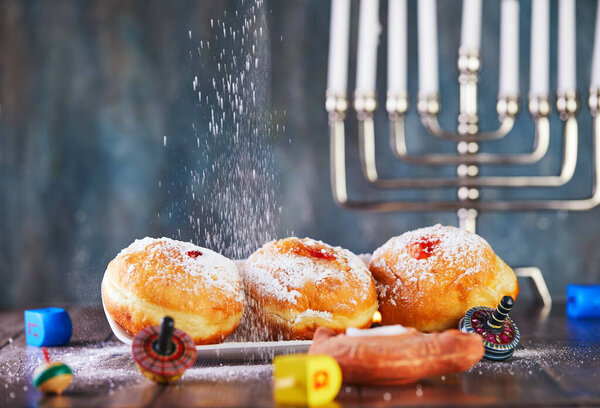Jewish holiday Hanukkah background. A traditional dish is sweet donuts. Hanukkah table setting a candlestick with candles and spinning tops on a blue background. Sprinkle donuts with powdered sugar