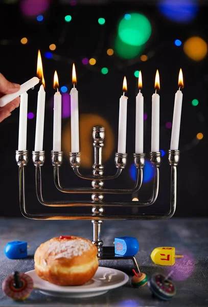 Jewish holiday Hanukkah background. A traditional dish is sweet donuts. Hanukkah table setting a candlestick with candles and spinning tops on a blue background. Lighting Chanukah candles. Copy space