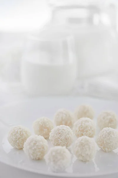 Witte chocolade snoepjes met kokosvulling met melk en kwark op de achtergrond op een witte achtergrond. Hoge sleutel foto — Stockfoto