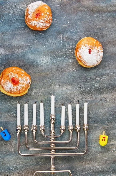 Jewish holiday Hanukkah background. A traditional dish is sweet donuts. Hanukkah table setting a candlestick with candles and spinning tops on a blue background. Flat lay. Copy space