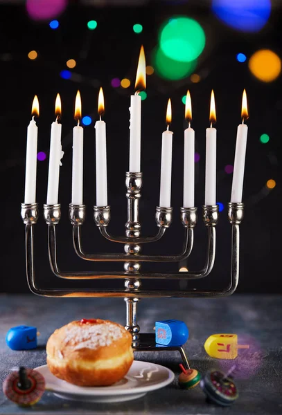 Jewish holiday Hanukkah background. A traditional dish is sweet donuts. Hanukkah table setting a candlestick with candles and spinning tops on a blue background. Lighting Chanukah candles. Copy space