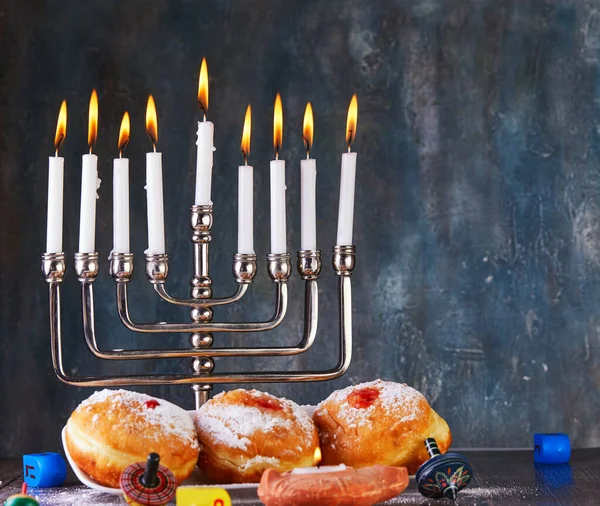 Jewish holiday Hanukkah background. A traditional dish is sweet donuts. Hanukkah table setting a candlestick with candles and spinning tops on a blue background. Copy space