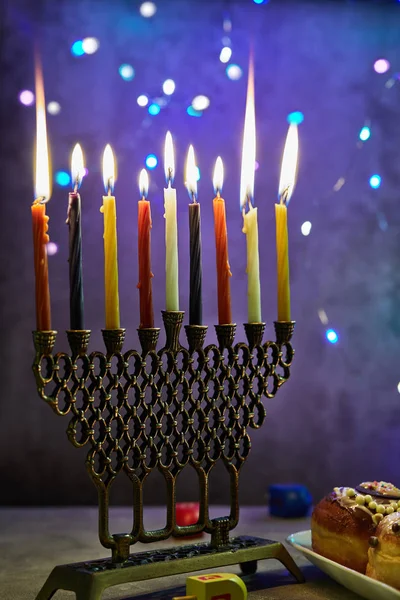 Jewish holiday Hanukkah background. A traditional dish is sweet donuts. Hanukkah table setting a candlestick with candles and spinning tops on a blue background. Lighting Chanukah candles