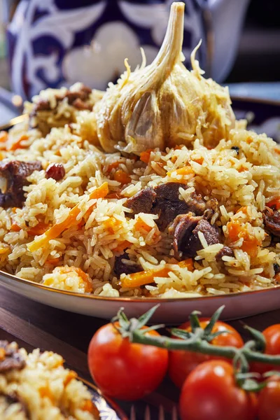 Uzbek pilaf in an authentic blue and gold dish, shot on a blue background with tomatoes, garlic and tea — Stock Photo, Image