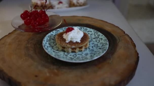 Una torta di waffle belgi e biscotti con panna montata e ciliegie in zucchero in cima si trova su un piatto, avvicinandosi e allontanandosi dalla macchina fotografica. — Video Stock