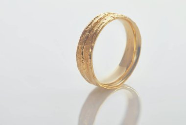 Mücevher yapımı. Beyaz arka planda duran sıra dışı bir dokusu olan sarı altın alyans.