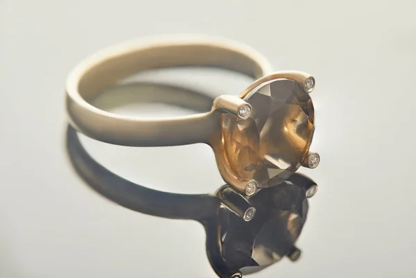 Smyckestillverkning. 18k gult guld ring med diamanter och topaz rök ligger på en grå bakgrund med reflektion — Stockfoto