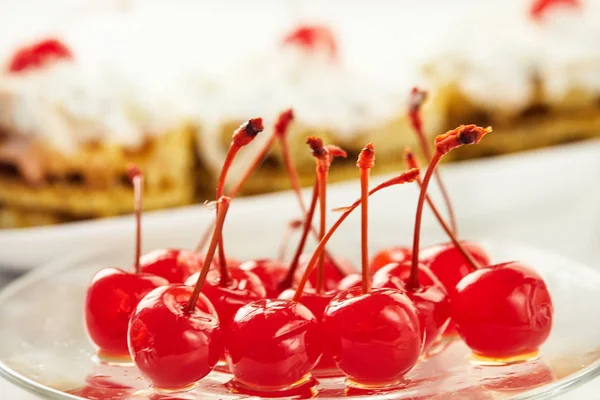 Wiśnia w cukrze z gałązkami na przezroczystej talerzu, na tle ciastek na jasnym tle — Zdjęcie stockowe