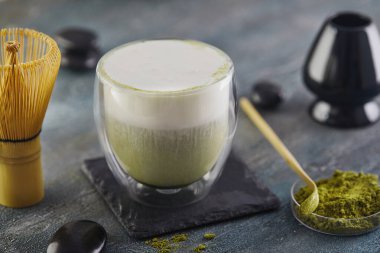 Mavi-gri arkaplanda kibrit yeşil çay. Çayı şapel ve bambu kaşığıyla eşleştir.