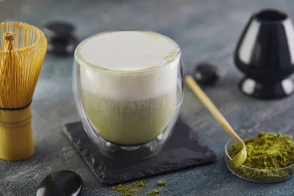 Mavi-gri arkaplanda kibrit yeşil çay. Çayı şapel ve bambu kaşığıyla eşleştir.