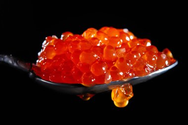 Siyah arka planda kırmızı havyar dolu bir kaşık..