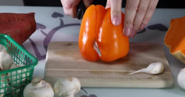 Mujer rebanadas de pimienta naranja en una tabla de madera en la cocina. Las manos femeninas preparan una ensalada con pimientos. Concepto de alimentación saludable — Vídeo de stock