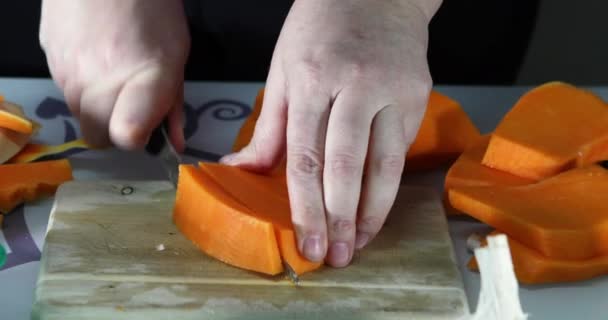 Woman slices a pumpkin on a wooden board in the kitchen. Female hands prepare cream soup with pumpkin. Healthy eating concept — Stock Video