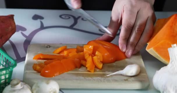 Mujer rebanadas de pimienta naranja en una tabla de madera en la cocina. Las manos femeninas preparan una ensalada con pimientos. Concepto de alimentación saludable — Vídeo de stock