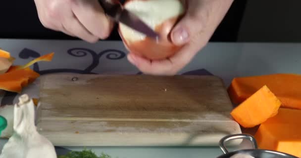 Žena loupe cibuli na dřevěné desce v kuchyni. Samičí ruce připravují smetanovou polévku s dýní a cibulí. Zdravý stravovací koncept — Stock video