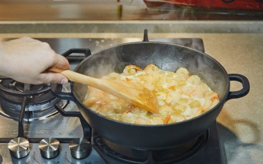 Bir kadın, tavada yağda kızartılmış karides küreklerini ahşap spatulayla karıştırıyor.