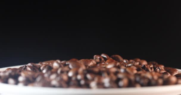 Pachnące ziarna kawy wpadają do talerza z innymi ziarnami na czarnym tle — Wideo stockowe