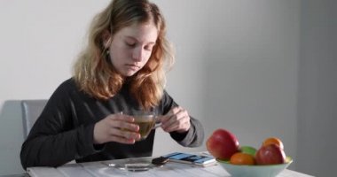 Genç bir kız cep telefonuna bakar ve masada kurabiyelerle çay içer..