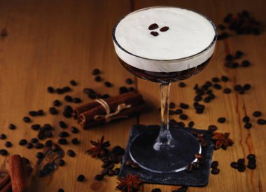 Kahve taneleri, tarçın ve ahşap arka planda yıldız anasonlu bir bardakta espresso martini kokteyli..