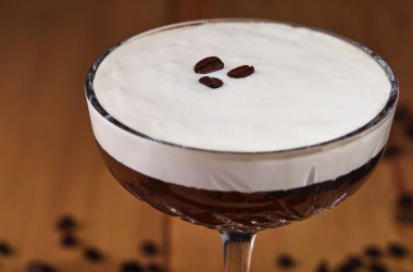 Kahve taneleri, tarçın ve ahşap arka planda yıldız anasonlu bir bardakta espresso martini kokteyli.