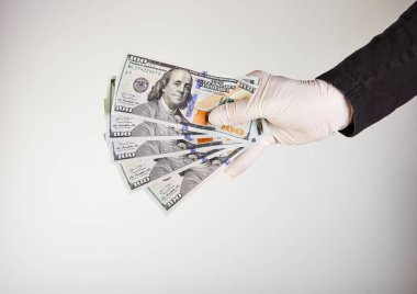 Beyaz eldivenli bir adamın elinde 100 dolarlık banknotlar halinde para var. Virüs ve bakterilere karşı koruma. Kavram. Covid-19 veya Coronavirus.