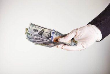 Beyaz eldivenli bir adamın elinde 100 dolarlık banknotlar halinde para var. Virüs ve bakterilere karşı koruma. Kavram. Covid-19 veya Coronavirus.