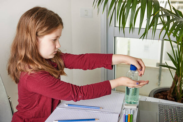 Дистанционное обучение онлайн. Школьница учится дома с ноутбуком и делает домашнюю работу в школе. Натирает руки о коронавирус гелем с алкоголем 70 процентов
