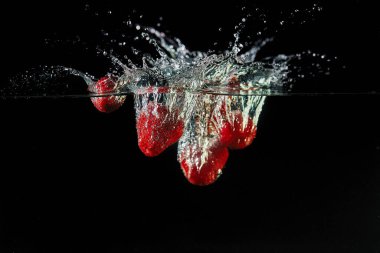 Çilekleri suya düşürmek, tasarım için sprey sıkmak, hareket halinde donmak. Su sıçraması ve siyah bir arka planda izole edilmiş sebzeler.