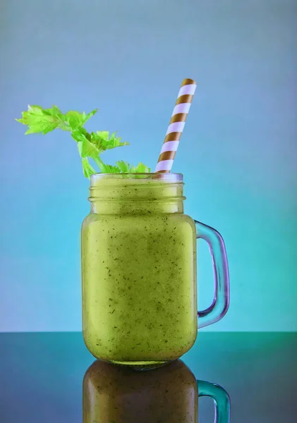 Healthy green smoothie, healthy eating and nutrition, lifestyle, vegan, alkaline, vegetarian concept. Green smoothie with organic ingredients, vegetables on a blue background with reflection.