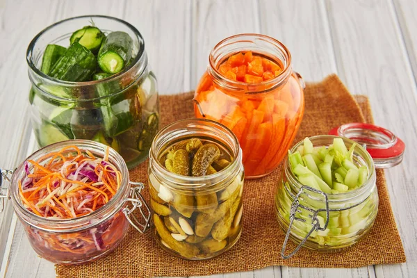 Fermented preserved vegetarian food concept. Sour sauerkraut, pickled carrots, pickled cucumbers, pickled celery in glass jars on a white wooden kitchen table. The concept of canned food. Copy space