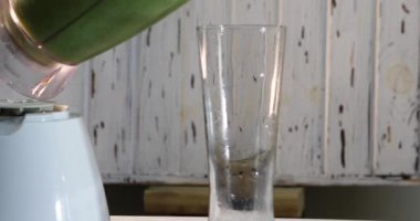 Ev sahibesi bardağa blenderdan yeşil meyve suyu doldurur..