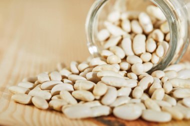 Beyaz fasulye tohumları cam bir kavanozdan ahşap bir zemine döküldü. Kapatın. Sağlıklı yeme kavramı.