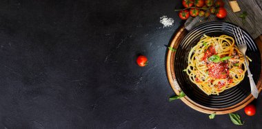 Lezzetli iştah açıcı klasik İtalyan makarnası domates soslu, parmesanlı ve fesleğenli karanlık bir masada. Üst manzara, yatay. Düz yatıyordu. Uzayı kopyala Pankart