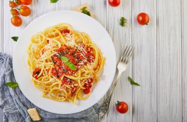 Lezzetli iştah açıcı klasik İtalyan makarnası domates soslu, parmesanlı ve fesleğenli beyaz ahşap bir masada. Üst manzara, yatay. Düz yatıyordu. Boşluğu kopyala.
