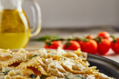 Krema soslu ravioli, kiraz domatesleri, ayçiçeği yağı ve açık ahşap arka planda fesleğen. Uzayı kopyala Yan görünüm.