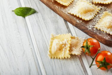 Unlu çiğ ravioli, kiraz domatesleri, ayçiçeği yağı ve açık ahşap arka planda fesleğen. İtalyan mantısı yapma süreci. Uzayı kopyala Yan görünüm.