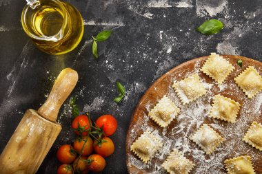 Unlu çiğ ravioli, kiraz domatesleri, ayçiçeği yağı ve koyu arkaplanda fesleğen. İtalyan mantısı yapma süreci. Uzayı kopyala Düz yatıyordu