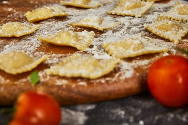 Unlu çiğ ravioli, kiraz domatesleri, ayçiçeği yağı ve koyu arkaplanda fesleğen. İtalyan mantısı yapma süreci. Yan görünüm.