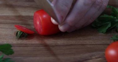 Kadın tahtada taze bir kiraz domatesi dilimliyor.