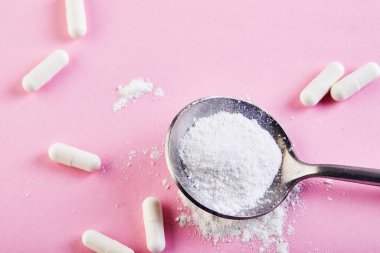 Kolajen tozu ve pembe arka planda haplar. Fazladan protein alımı. Deri, kemik, eklem ve bağırsaklar için doğal kozmetik takviyesi. Bitki ya da balık bazlı. Yan görüş. Boşluğu kopyala