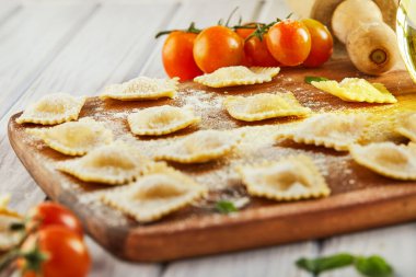 Unlu çiğ ravioli, kiraz domatesleri, ayçiçeği yağı ve açık ahşap arka planda fesleğen. İtalyan mantısı yapma süreci. Uzayı kopyala Yan görünüm.
