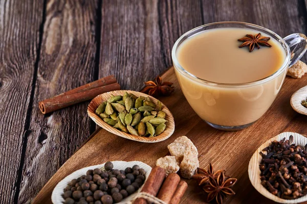 Traditional Indian drink - masala tea with spices. Cinnamon, cardamom, anise, sugar, cloves, pepper on a dark wooden background. Copy space. Side view