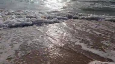 HD Video Manzarası, günbatımında kumlu bir plaja karşı mavi deniz suyu dalgalarının geniş bir görüntüsü ve spor yapan insanların siluetleri..