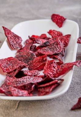 Diyet sağlıklı yeme konsepti. Kurumuş pancar cipsi ya da beyaz dikdörtgen bir tabakta pişmiş pancar, gri beton arka planda. Organik doğal gıdalar. Boşluğu kopyala.