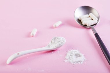 Kolajen tozu ve pembe arka planda haplar. Fazladan protein alımı. Deri, kemik, eklem ve bağırsaklar için doğal kozmetik takviyesi. Bitki ya da balık bazlı. Yan görüş. Boşluğu kopyala