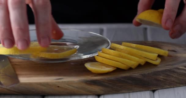 Mężczyzna kładzie plasterki cytryny na przezroczystym talerzu do serwowania na drewnianym tle. 4k wideo — Wideo stockowe