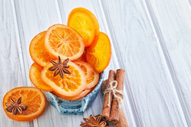 Açık arkaplanda mavi bir kasede anason ve tarçınlı kuru portakal dilimleri veya mandalinalar. Vejetaryenlik ve sağlıklı beslenme. Boşluğu kopyala.