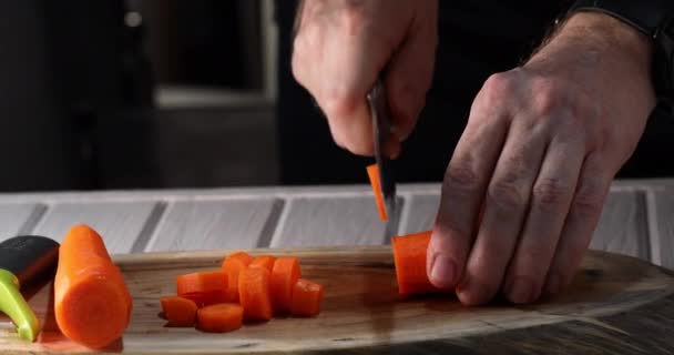 Un homme tranche une carotte en tranches sur un fond de bois. Vidéo 4k — Video